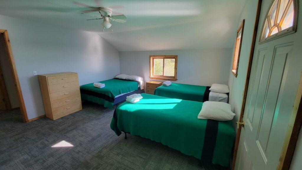 Three matching twin size beds in a bright, clean bedroom. Grey flooring and white walls let the green bedding pop.