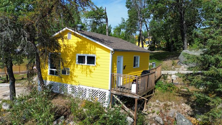 A yellow cabin at the water's edge with rocks and trees around it