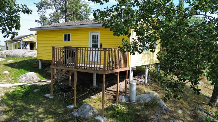 Yellow cabin at Separation Lake Lodge that has a small deck off the front of the cabin with the lodge's store in the background.