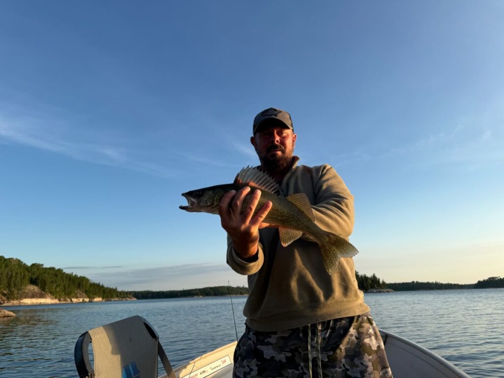 Man holding up a fish that will probably be his supper walleye and the fish has his fins up on his back and the sunset is just starting