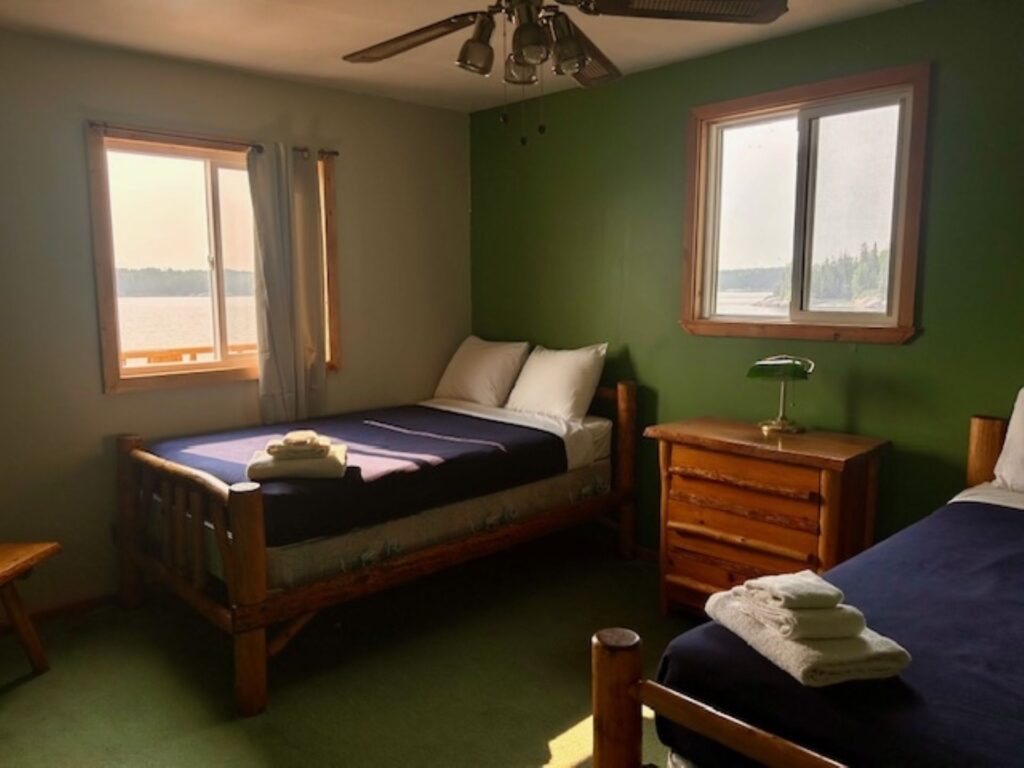Rental cabin bedroom for a fisherman with 2 beds and a dresser while seeing the lake views from 2 bedroom windows